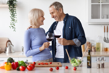 Romantic senior spouses drinking wine while cooking together