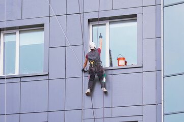 A window cleaner works on the facade of a high-rise office building. Industrial alpinism. Young man points up. Individual safety system for an industrial climber.