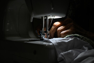 Close up hand sewing with a machine in dim light.