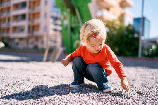 Little girl squatting picking pebbles with a stick. High quality photo