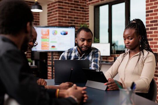 African American People Brainstorming Ideas In Meeting, Using Laptop And Tablet To Create Online Presentation With Data Research And Information. Analyzing Documents And Files To Send Email Report.