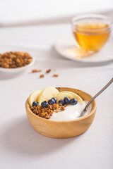 Granola with fresh blueberries and yogurt in a wooden bowl on a white tablecloth. Useful breakfast.