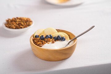 Granola with fresh blueberries and yogurt in a wooden bowl on a white tablecloth. Useful breakfast.