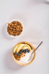 Granola with fresh blueberries and yogurt in a wooden bowl on a white tablecloth. Useful breakfast.