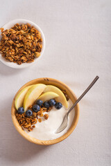 Granola with fresh blueberries and yogurt in a wooden bowl on a white tablecloth. Useful breakfast.