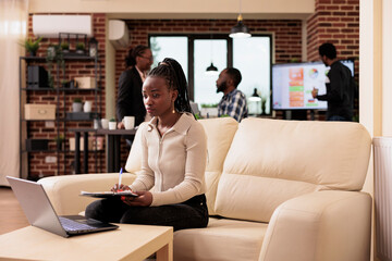 Business woman taking notes on documents and using laptop in startup office, working on reseach data and analysis report. Doing paperwork and sending professional email to project manager.