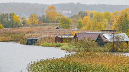 Rundown boat houses, with their entrances grown over with reeds, sit among the beauty of autumn colors on a lake.