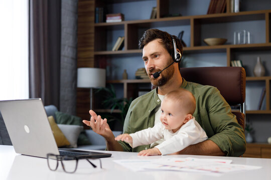Father on maternity leave, holding an online conference, a meeting in the home office with a small child in his arms. Dad with a child. Freelancer combines child care and work. Paternity leave