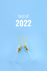 Words Best of 2022 and two champagne glasses on blue background decorated with golden starry...