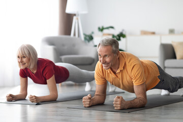 Cheerful senior couple having workout at home, planking