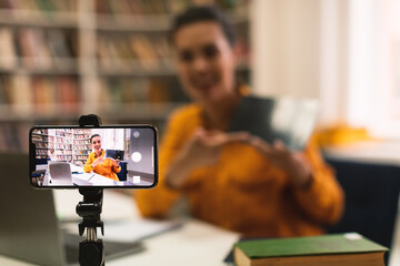 Female teacher shooting online lecture to students using cellphone on tripod and showing tablet, selective focus - obrazy, fototapety, plakaty