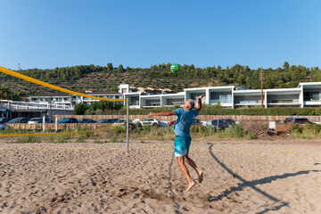 Shot of a mature volleyball player jumping against the net to hit the ball in sunlight.Popular outdoor sport for people.