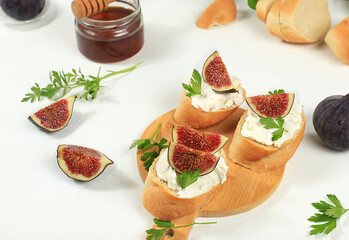Healthy breakfast with ingredients, toast with figs and soft cream cheese and honey, Canape or crostini with fried baguette and herbs on a light sunny table, italian recipes menu, selective focus