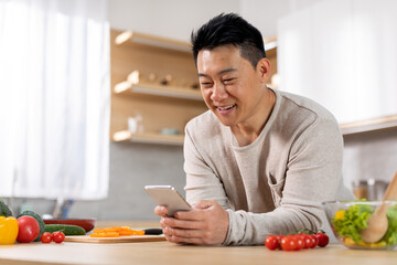 Positive asian man checking mobile app to learn cooking