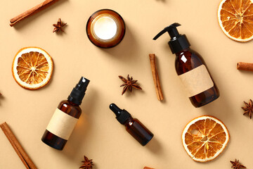Amber glass cosmetics bottles with dried orange slices, cinnamon sticks, anise stars on beige...