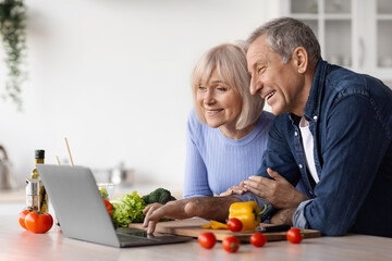 Cheerful senior couple watching food vlog while cooking, copy space
