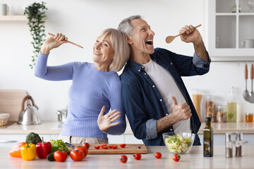 Senior husband and wife having fun while cooking, singing songs