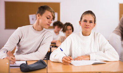 Portrait of teenage school girl and boy sitting together in classroom during lesson in secondary school