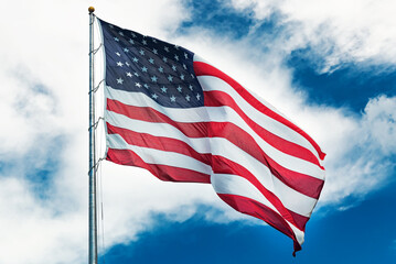 Obraz premium Large American flag waving in the wind against a cloudy blue sky.