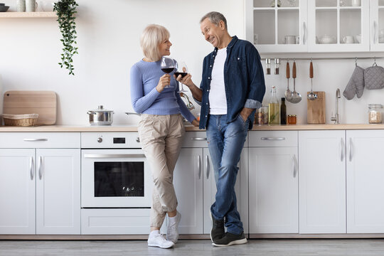 Happy Senior Couple Drinking Red Wine At Kitchen, Full Length