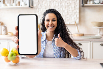 Online Offer. Joyful Young Woman Sitting In Kitchen And Showing Blank Smartphone