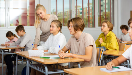 Fototapeta premium Teenagers sitting at desks in classroom during lesson and doing tasks.