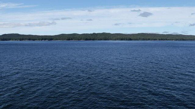 Dark calm blue waters of the Alaska Inside Passage accent the forested pine-tree lined shores in the distance
