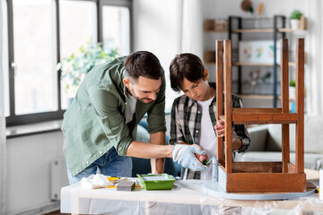 renovation, diy and home improvement concept - father and son in gloves with paint roller painting old wooden table in grey color