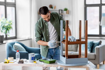 furniture renovation, diy and home improvement concept - man in gloves with paint brush painting...