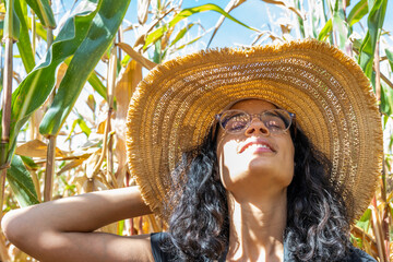 femme souriante avec un chapeau de paille dans un champs de mais au soleil