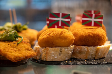 Typical snack in bars of Basque Country, pinchos or pinxtos, small fried croquette with squid and flag of Basque Country, San Sebastian, Spain
