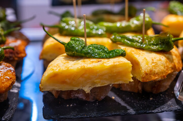 Typical snack in bars of Basque Country, pinchos or pinxtos, small slices of bread withn different toppings and fastened with skewers, San Sebastian, Spain. Potato tortilla with green pepper.