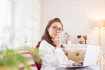 部屋でラップトップコンピューターを見るシニア女性　考える