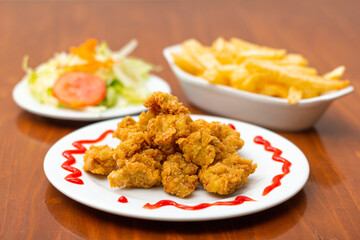 Chicken chicharron, accompanied by French fries and salad on a wooden table.