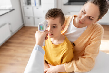 Obraz na płótnie Canvas medicine, healthcare and pediatry concept - mother with sick little son and doctor measuring temperature with infrared forehead thermometer at clinic