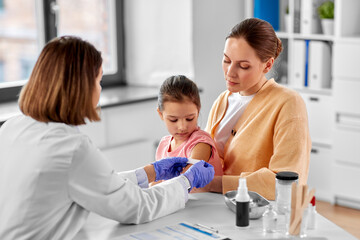 Fototapeta premium medicine, healthcare and pediatry concept - female doctor or pediatrician attaching medicinal patch to arm of little girl patient with mother at clinic