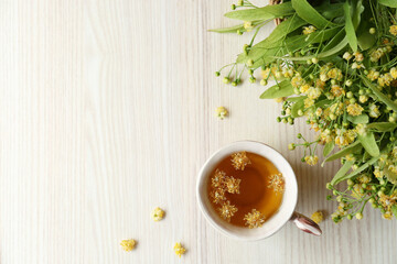 Cup of aromatic tea with linden blossoms on white wooden table, flat lay. Space for text