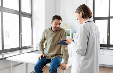 medicine, healthcare and people concept - female doctor with clipboard and happy smiling man...