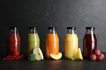 Bottles with delicious colorful juices and fresh ingredients on black table