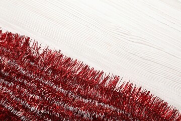Shiny red tinsel on white wooden background, flat lay. Space for text