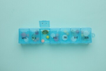 Plastic box with different pills on light blue background, top view