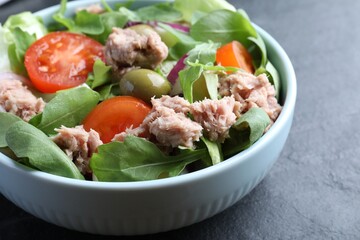 Bowl of delicious salad with canned tuna and vegetables on black table, closeup