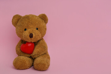 Cute teddy bear with red heart on pink background, space for text. Valentine's day celebration