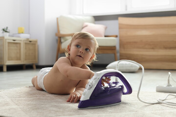 Cute baby playing with iron on floor at home. Dangerous situation