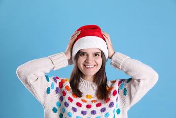 Pretty woman in Santa hat and festive sweater on light blue background