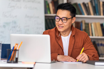 Japanese Male Tutor At Laptop Taking Notes Sitting At Workplace - obrazy, fototapety, plakaty