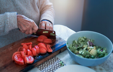 view of senior woman's hands cutting tomato on a wooden board in the kitchen