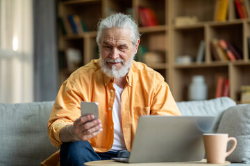 Happy senior businessman working from home, using laptop and phone