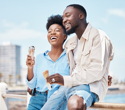 Happy Couple At The Beach Eating An Ice Cream Cone While On A Date In Nature While On Spring Vacation. Black Man And Woman Talking And Laughing While Hugging And Having Dessert On Holiday By Seaside.