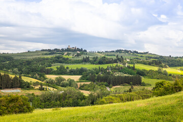 Fototapeta na wymiar Rural view of Tuscany with rolling green hills and traditional Tuscan architecture on a partly sunny day.